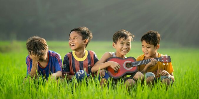 four boys laughing and sitting on grass during daytime