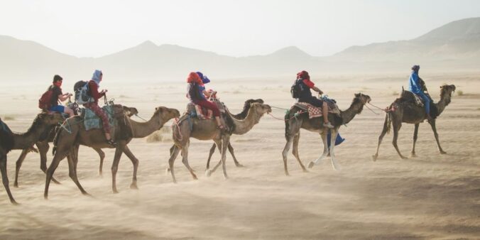 group of people riding camel on sand dune